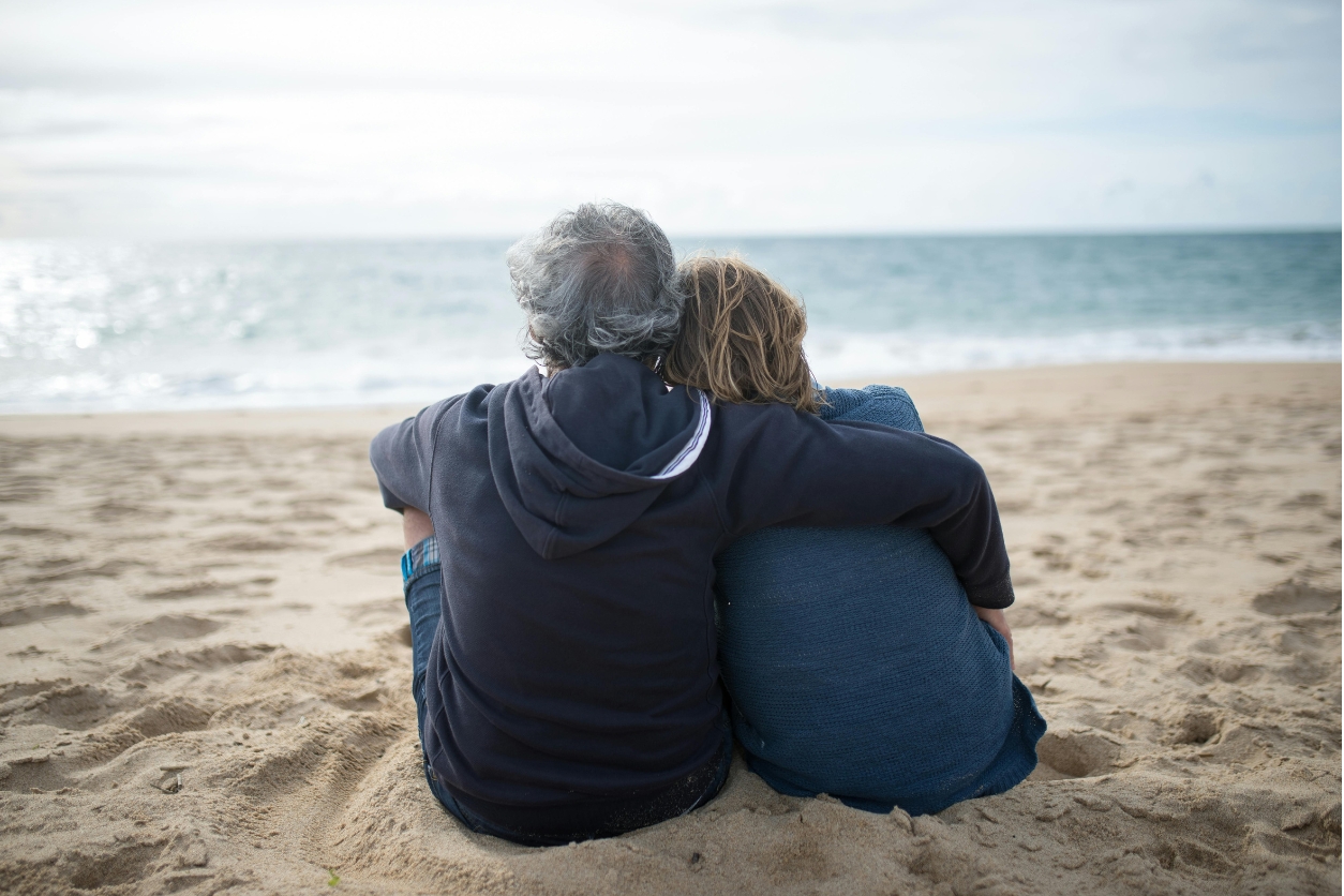 senior couple sitting on beach embracing