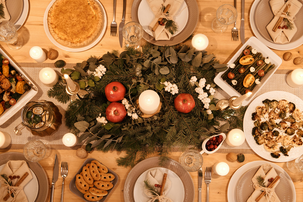 pexels nicole michalou 5779183A Christmas dinner table set with plates and a centrepiece of greenery and candles, shot from overhead